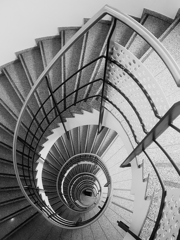 Escalier en colimaçon vu du dessus dans un bâtiment moderne, avec marches en pierre et garde-corps en métal. Escalier en colimaçon vu du dessus dans un bâtiment moderne, avec marches en pierre et garde-corps en métal.