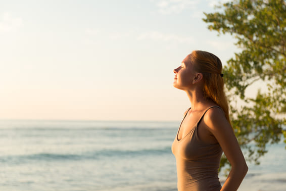 Femme de profil respirant face à la mer au lever du soleil, le visage tourné vers le ciel, avec la silhouette d'un arbre en arrière-plan. Femme de profil respirant face à la mer au lever du soleil, le visage tourné vers le ciel, avec la silhouette d'un arbre en arrière-plan.